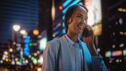 Beautiful Young Woman Talking on Smartphone Walking Through Night City Street Full of Neon Light. Portrait of Gorgeous Smiling Female Answering Mobile Phone in Stylish Urban Area.