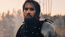 Handsome Medieval Knight King on Battlefield, Looking at Camera. Portrait of Mighty Warrior Soldier Contemplating Victory. War, Invasion, Conquest. Dramatic Scene in Cinematic Historic Reenactment