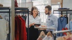 Clothing Store: Businesswoman Uses Tablet Computer, Talks to Visual Merchandising Specialist, Collaborate To Create Stylish Collection. Small Business Fashion Shop Sales Manager Talks to Designer