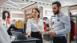 Clothing Store: Businesswoman Uses Laptop Computer, Talks to Visual Merchandising Specialist, Collaborate To Create Stylish Collection. Business Owner's Fashion Shop: Sales Manager Talks to Designer