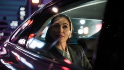 Beautiful Businesswoman is Commuting from Office in a Backseat of Her Luxury Car at Night. Entrepreneur Passenger Traveling in a Transfer Taxi in Urban City Street with Working Neon Signs.