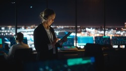 Caucasian Female Air Traffic Controller Working on Tablet in Airport Tower. Office Room is Full of Desktop Computer Displays with Navigation Screens, Airplane Flight Radar Data for the Team.