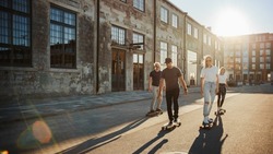 Group of Girls and Boys on Skateboards Through Fashionable Hipster District. Beautiful Young People Skateboarding Through Modern Stylish City Street During Golden Hour.