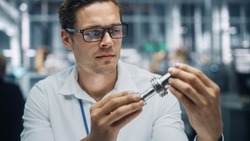 Close Up Portrait of Young Handsome Engineer in Glasses Working on Manufacturing Metal Parts in Office at Car Assembly Plant. Industrial Product Designer Examining Prototype Parts Before Production.