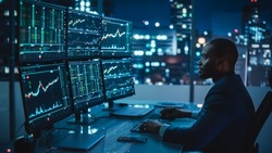 Financial Analyst Working on Computer with Multi-Monitor Workstation with Real-Time Stocks, Commodities and Exchange Market Charts. African American Trader Works in Investment Bank Late at Night.
