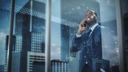 Portrait of Successful African-American Businessman Standing in Office, Making Phone Call to Close the Deal, Looking out of Window. Successful Stock Market Investor Making e-Business. Outside Shot