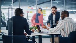 Diverse Modern Office: Muslim Businesswoman Wearing Hijab and Stylish Hispanic Entrepreneur Lead Business Meeting, Use Laptop, Talk, Brainstorm with Managers. Young Professionals on e-Commerce Project