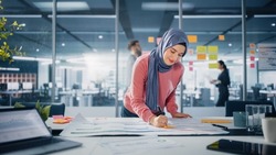 Modern Office: Portrait of Muslim Businesswoman Wearing Hijab Works on Engineering Project, Does Document and Blueprints Analysis. Empowered Digital Entrepreneur Works on e-Commerce Startup Project
