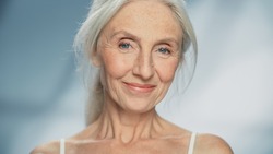 Close-up Portrait of Beautiful Senior Woman Looking at Camera and Smiling Wonderfully. Gorgeous Elderly Lady with Natural Lush Grey Hair, Blue Eyes. Beauty and Dignity of Old Age
