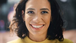 Close-up Portrait of Gorgeous Dark Haired Hispanic Woman with Deep Brown Eyes Looking at Camera, Smiling Charmingly. Happy Young Latin Woman Enjoys Life with Fun, Success. Background Bokeh City Street