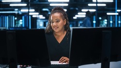 Portrait of African American Female IT Specialist Working on Desktop in Data Center. System Administrator Works on Web Services, Cloud Computing, Server Analytics, Cyber Security Maintenance, SAAS