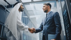 Businessman Talking with Arab Investment Partner while Riding Glass Elevator to Office in a Modern Business Center. International Corporate Associates Shake Hands and Agree on a Deal in a Lift.