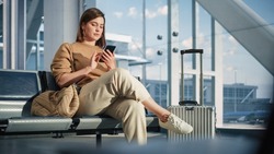 Airport Terminal: Woman Waits for Flight, Uses Smartphone, Browse Internet, Social Media, Online Shopping. Traveling Female Remote Work Online on Mobile Phone in a Boarding Lounge of Airline Hub