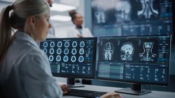 Medical Hospital Health Care Lab: Camera Captures Professional Neuroscientists Analysing CT Scan Finding Cure for Sick Patient and Female Neurologists Using Computer with Brain Scan MRI Images
