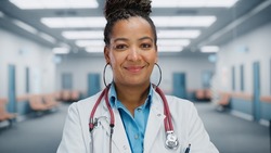Close Up Portrait of African American Female Medical Doctor with Stethoscope Standing in Hospital Hallway. Successful Black Physician in White Lab Coat Looks at the Camera, Smiles. Ready to Save Lives