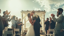 Beautiful Bride and Groom Celebrate Wedding Outdoors on a Beach Near the Ocean. Perfect Marriage Venue with Best Multiethnic Diverse Friends Throwing Flower Petals on the Newlyweds.