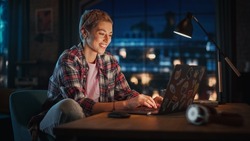 Young Attractive Woman Using Laptop Computer in Stylish Loft Apartment in the Evening. Creative Female Smiling, Checking Social Media, Browsing Internet. Urban City View from Big Window.