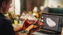 Inspired Blonde Man Creating Custom Made Model of Shoes and Looking at 3D Prototype Made in Editing Software on his Laptop. Arts and Unique DIY Objects For Personal Style Concept.
