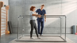 Physical Therapy Sports Center: Portrait of Strong Middle Aged Female Patient with Injury Successfully Walks Holding Parallel Bars. Physiotherapist, Rehabilitation Hospital Doctor, Medical Help.