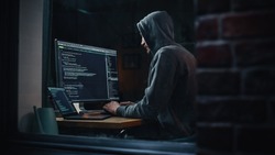 Night Apartment: Evil Greedy Hacker Wearing Hoodie, Breaks into Data Servers, Does DDOS Attack, Phishing Scheme, Malware, Sends Virus. Cyber Security and Crime Concept. View From Outdoors into Window.