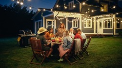 Parents, Children and Friends Gathered at a Barbecue Dinner Table Outside a Beautiful Home with Lights Decorations. Old and Young People Have Fun and Eat Meals. Garden Party Celebration in a Backyard.