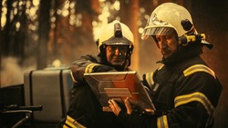 Close Up Portrait of Two Professional Firefighters Standing Next to an All-Terrain Vehicle, Using a Heavy-Duty Laptop Computer and Figuring Out a Best Strategy for Extinguishing the Wildland Fire.