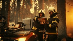 Portrait of Two Professional Firefighters Standing Next to an All-Terrain Vehicle, Using Heavy-Duty Laptop Computer and Figuring Out a Best Strategy for Extinguishing the Wildland Fire. Medium Shot.
