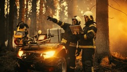 Portrait of Two Professional Firefighters Standing Next to an All-Terrain Vehicle, Using Heavy-Duty Laptop Computer and Figuring Out a Best Strategy for Extinguishing the Wildland Fire. Wide Shot.
