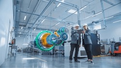 Factory Digitalization: Two Industrial Engineers Use Tablet Computer, Visualize 3D Model of Clean Green Energy Engine. Industry 4 High-Tech Electronics Facility with Machinery Manufacturing Products