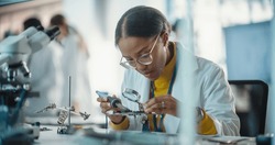 Portrait of Black Female Lab Specialist Carefully Soldering a Circuit Board in a Manufacturing Industrial Company. Professional Woman in Lab Coat Working on the Latest Technological Project