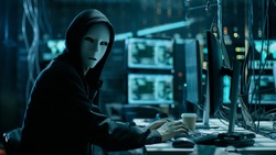Masked Hacker is Using Computer for Organizing Massive Data Breach Attack on Corporate Servers. They're in Underground Secret Location Surrounded by Displays and Cables.