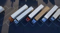 Aerial Top View of White Semi Truck with Cargo Trailer Parking with Other Trucks on Special Parking Lot.