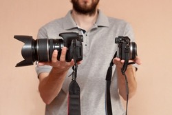 Man is holding in one hand dslr camera and mirrorless in another one. Comparison of two cameras for shooting. Choosing before buying and evaluating the pros and cons of cameras