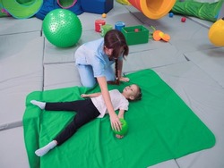 Physical therapist working with little girl in sensory room. Exercising with weighted ball and pressure to help kid relax in a therapy center. sensory integration session