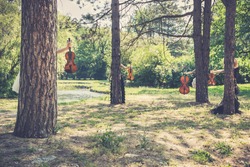 Music and nature concept. Female musical quartet with string instruments, one cello and three violins, hiding behind the trees, prepares to play in nature next to the river.
