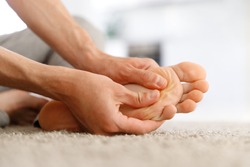 Man hands giving foot massage to yourself to relieve pain after a long walk, suffering with flat feet, close up, soft focus, indoors. Flat feet, leg fatigue.  