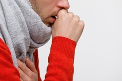 Close up of unhealthy man in orange sweater suffering with pulmonary cough due to cold, flu, respiratory infections, pneumonia, bronchitis, wrapped in scarf, isolated on white background. 