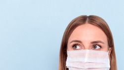Close up of woman wearing protective mask, looking aside at copy space, isolated on blue background. Flu, allergy, protection against virus, coronavirus pandemic - covid-19. Medical mask advertising
