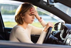 Exhausted woman driver feeling headache, sitting inside her car, keeping hand to head and feeling anxiety. Stop after driving car in traffic jam.Blood pressure