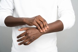 Closeup of African man arms touching painful wrist caused by prolonged work on computer, laptop. Black male suffering from carpal tunnel syndrome, arthritis, neurological disease. Numbness of hand.