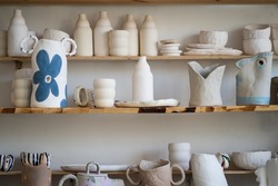 Handmade ceramic crockery and craft pottery jug, jars and cups standing on shelves in creative studio or potter store. Different handicraft clay earthenware bowls in artisan craftsman classes workshop