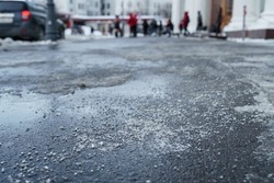 De-icing chemical reagent on the road will make the road safe in winter time. Pavement is sprinkled with technical salt, focus on foreground, people on blurred background. 