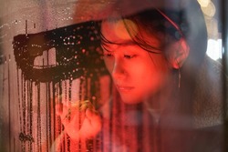Sensitive asian millennial girl suffer from solitude alone draw on wet glass in rain. Unhappy young woman emotional and nostalgic after breakup with boyfriend feeling bad depression and loneliness