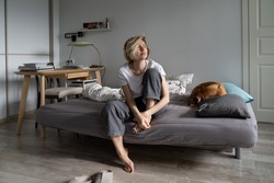 Loneliness at midlife. Thoughtful sad middle-aged Scandinavian woman sitting on sofa with dog looking in distance, suffering from depression, feeling lonely, pondering what is the point of life