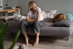 Lonely at 40. Sad single woman feel depressed while living alone, sitting on sofa with dog looking aside, thinking of life purpose, experiencing emotional pain after break up. Loneliness, depression