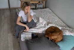 Unemployed mature woman regrets about difficult money problems and looks upset. Middle-aged female has absence of life sense but tries to think about life upgrading sitting on bed with sleeping dog