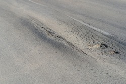 Broken road with holes and cracks built in countryside on hot sunny day. Deformed and expanded asphalt surface with potholes caused by heavy overloaded trucks driving on highway at rural site
