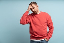 Worried man feeling heartbroken and stress put hand to forehead. Middle aged male isolated on studio blue background with expression of anxiety, detachment, shock, alienation, disappointment on face. 