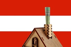 Euro bill in a chimney of a wooden toy symbolic house against the background of the Austria flag, copy space for text. Heating concept