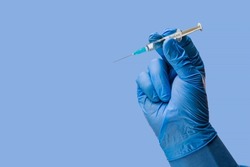 Doctors hand in surgical gloves holds a syringe on a classic symbolic blue background